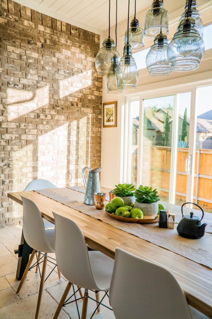 portfolio-02 Sunlit dining room with contemporary decor and a rustic brick wall, featuring stylish lighting and a wooden table.