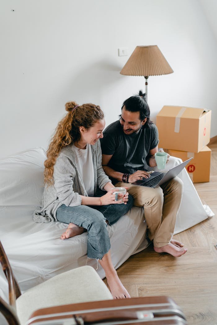 services-03 Joyful couple using a laptop and coffee in their new apartment, surrounded by moving boxes.